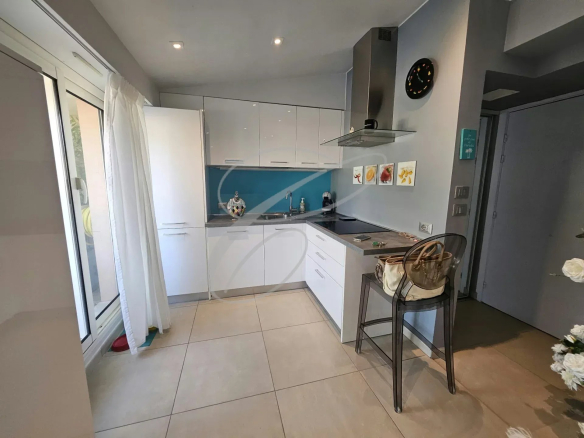 Cuisine moderne et rénovée d'un appartement à Menton, avec meubles blancs et plan de travail noir.