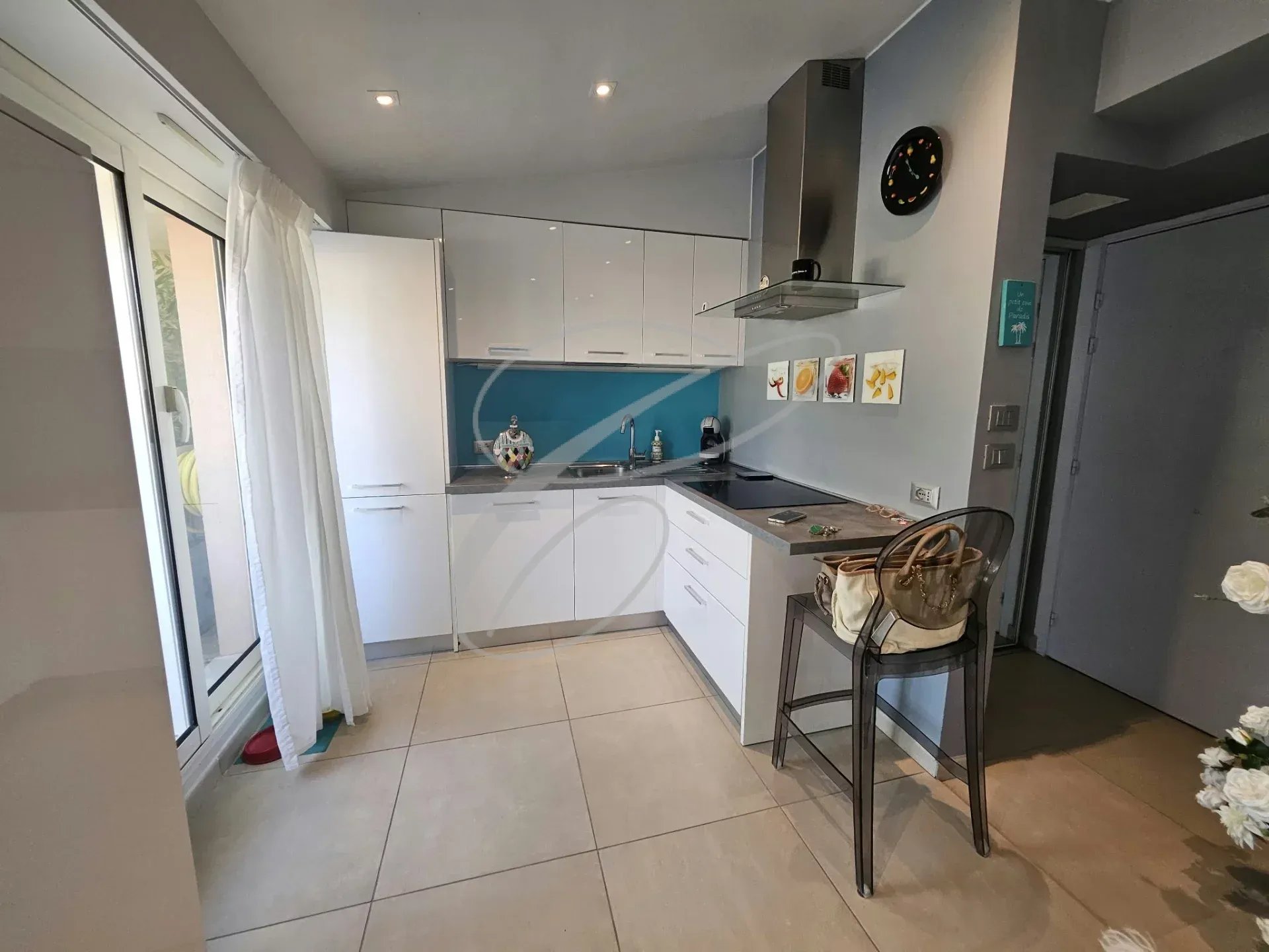 Cuisine moderne et rénovée d'un appartement à Menton, avec meubles blancs et plan de travail noir.