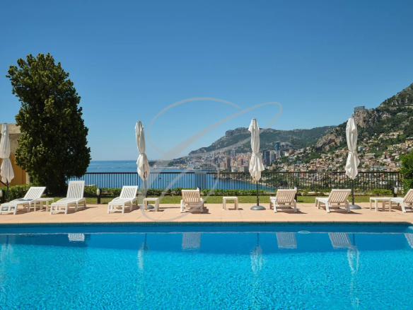 Vue de la piscine d'une résidence avec transats et vue panoramique sur la mer et Monaco.