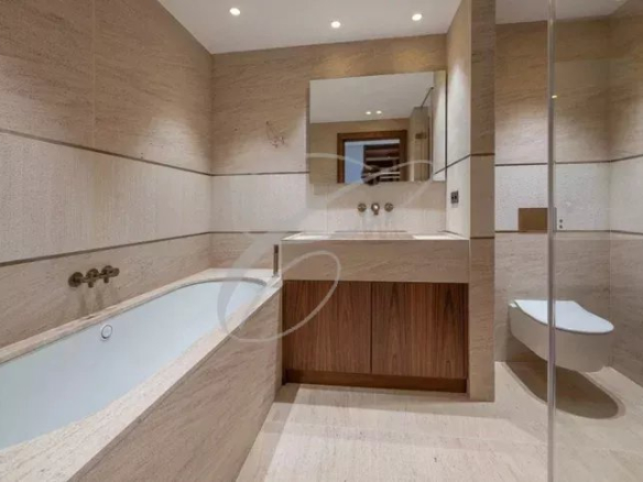 Salle de bain moderne avec baignoire et douche, murs en pierre beige, éclairage doux.
