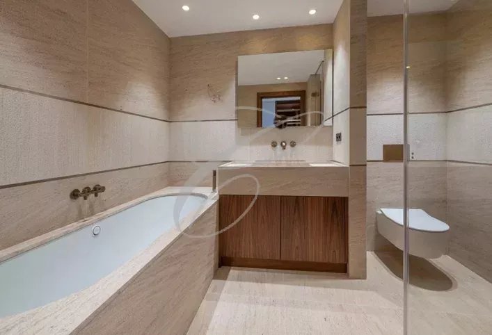 Salle de bain d’une villa à Nice Salle de bain moderne avec baignoire et douche, murs en pierre beige, éclairage doux.