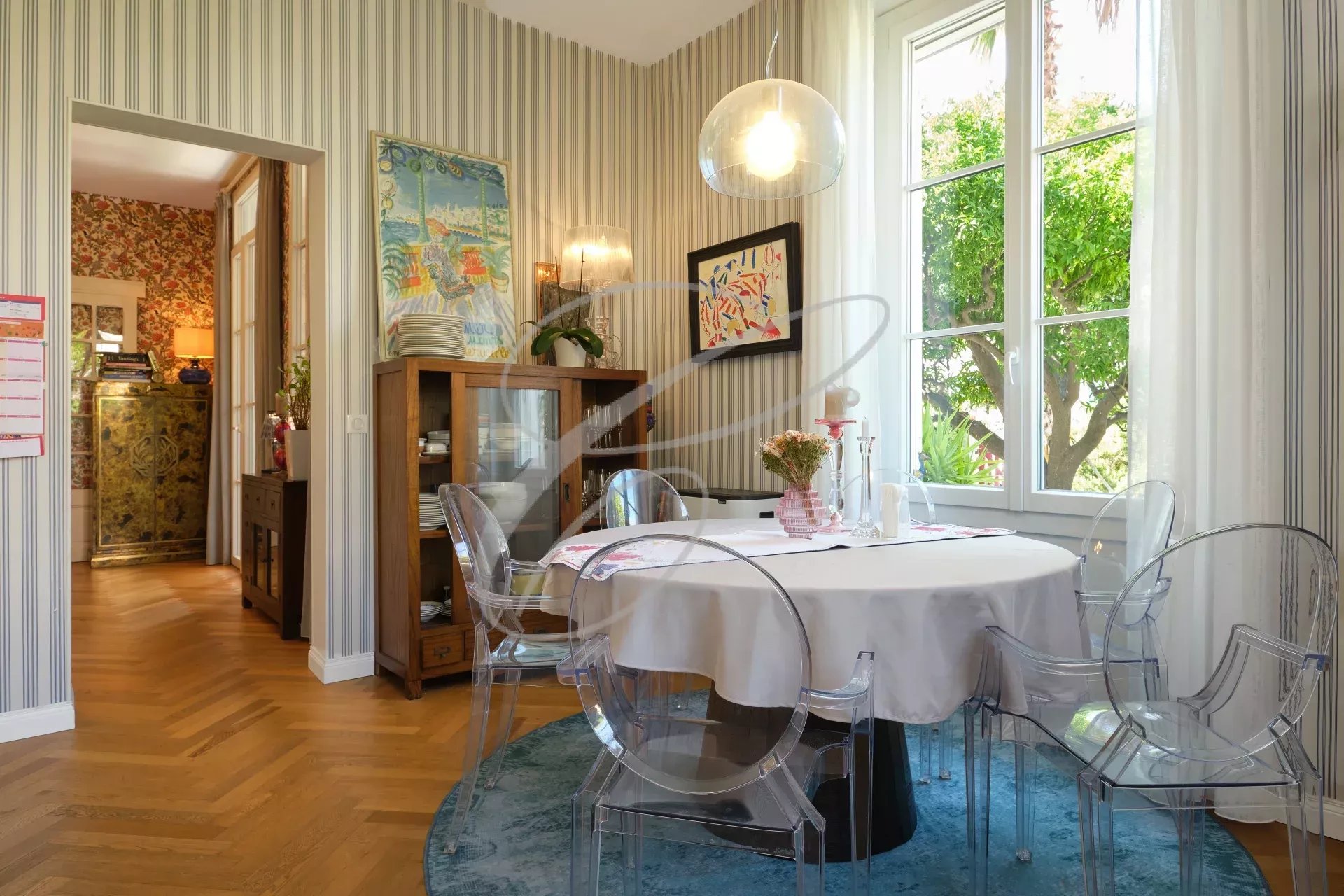 Salle à manger de la villa à Roquebrune-Cap-Martin Salle à manger d'une villa avec table ronde et chaises transparentes, fenêtres donnant sur un jardin.