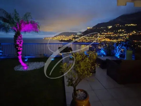 Terrasse d'un appartement avec vue sur la baie de Monaco, palmier illuminé et jardin.