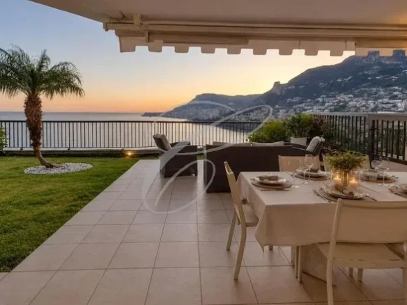 Terrasse d'un appartement avec vue sur la mer et les montagnes, mobilier de jardin et table dressée.
