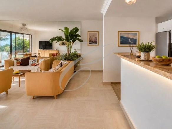 Intérieur d'un appartement moderne avec salon, cuisine ouverte et plantes, vue sur la mer.