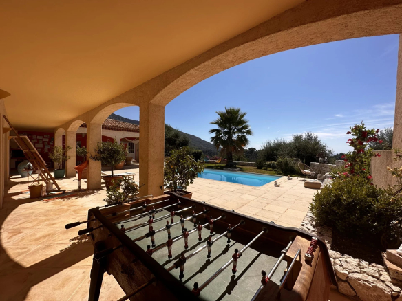 Vue d'une villa avec piscine et jardin, incluant une table de baby-foot sous une terrasse.