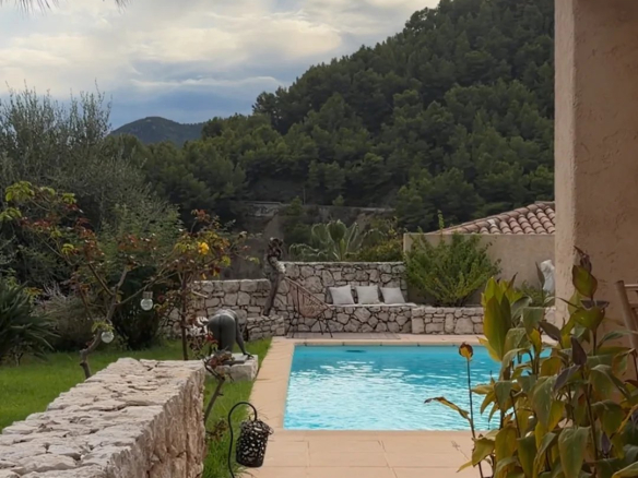 Vue sur la piscine et le jardin d'une villa à Sainte-Agnès, avec des montagnes en arrière-plan.
