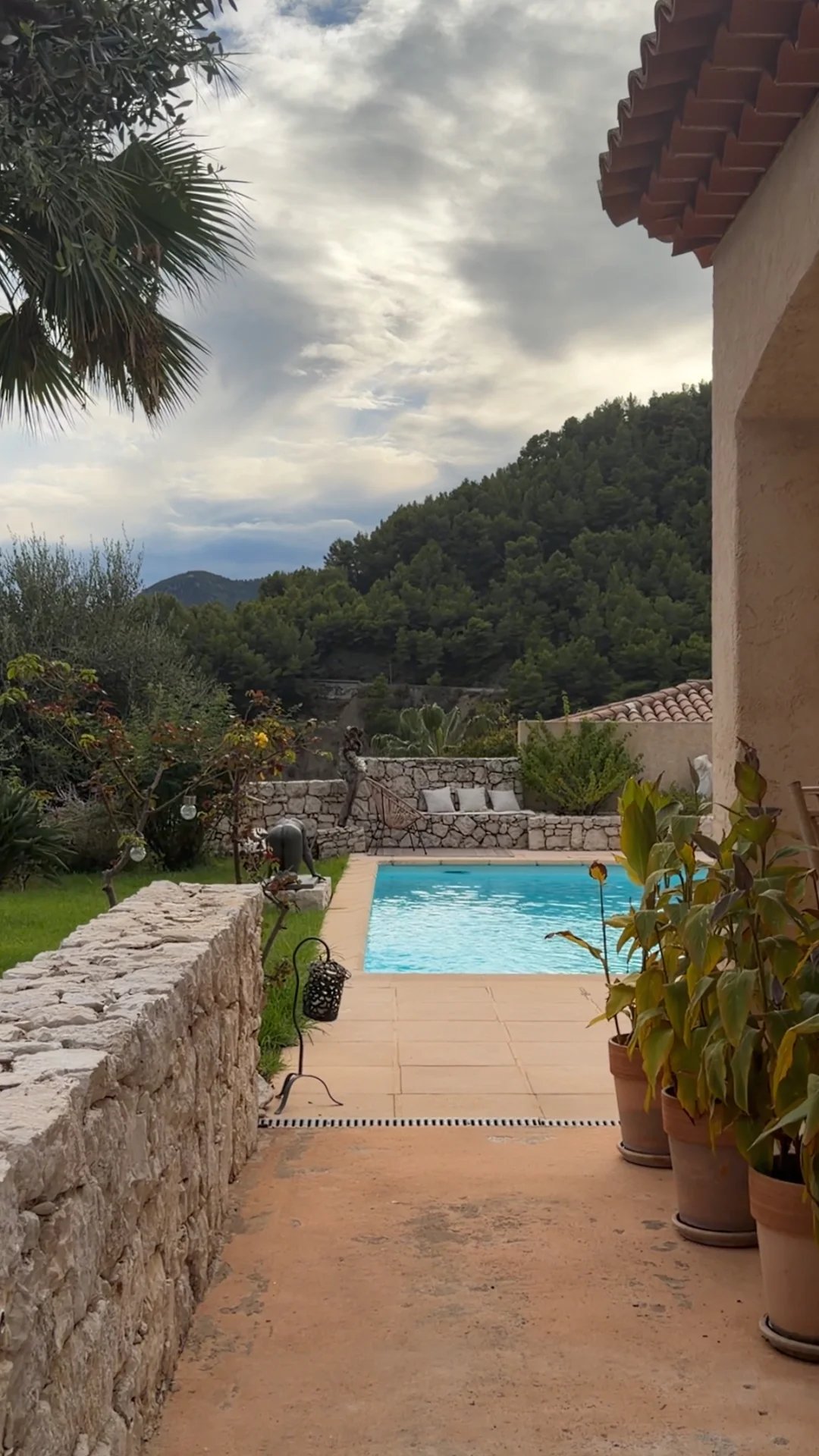 Vue sur la piscine et le jardin d'une villa à Sainte-Agnès, avec des montagnes en arrière-plan.