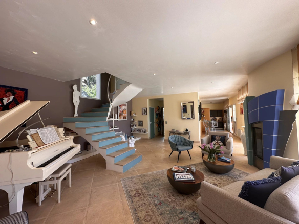 Intérieur d'une villa avec un salon spacieux, piano blanc et escalier menant à l'étage.