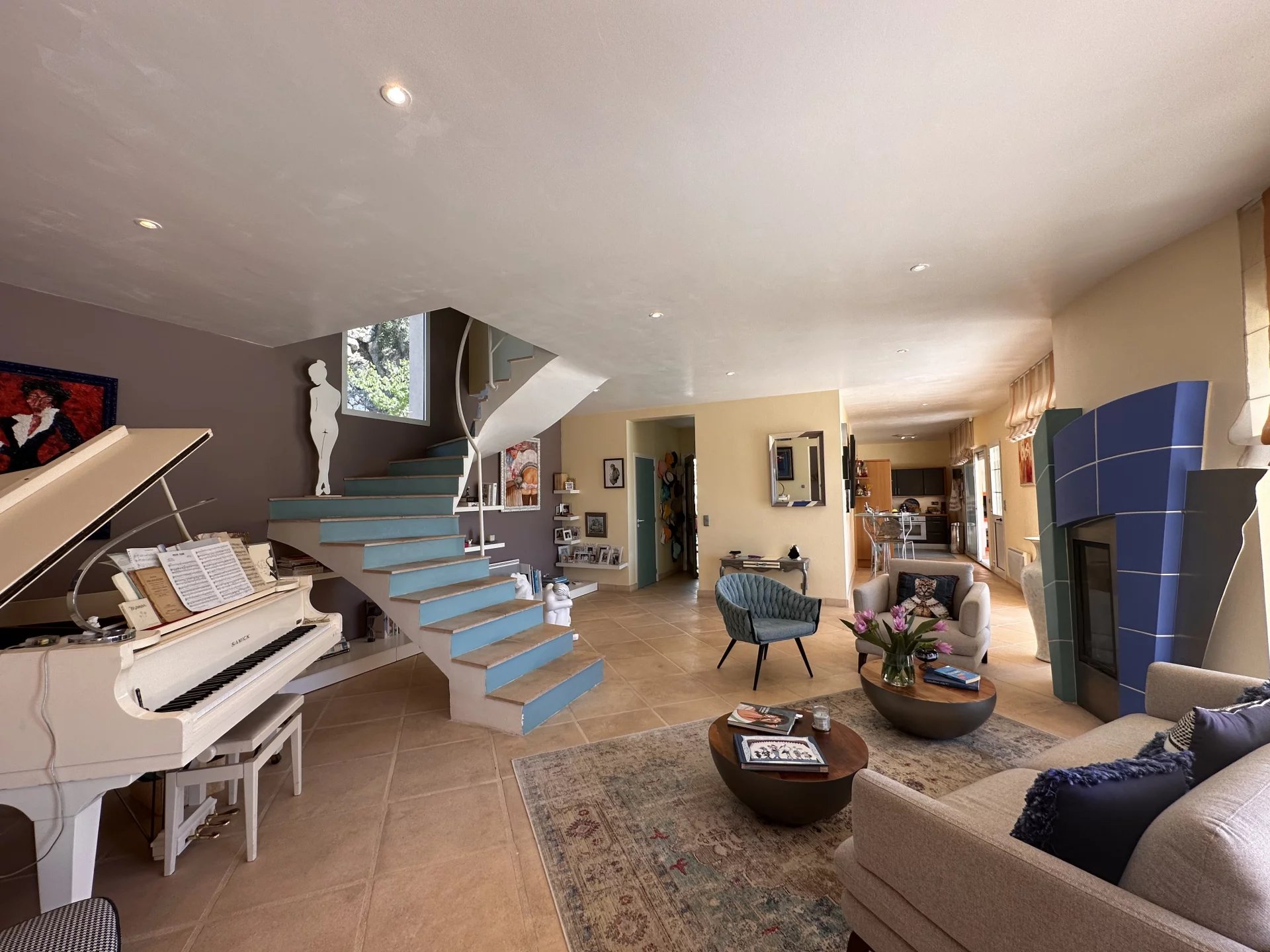 Intérieur d'une villa avec un salon spacieux, piano blanc et escalier menant à l'étage.