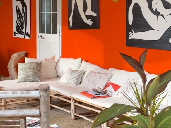 Intérieur d'une villa avec murs orange, œuvres d'art et mobilier en bambou.