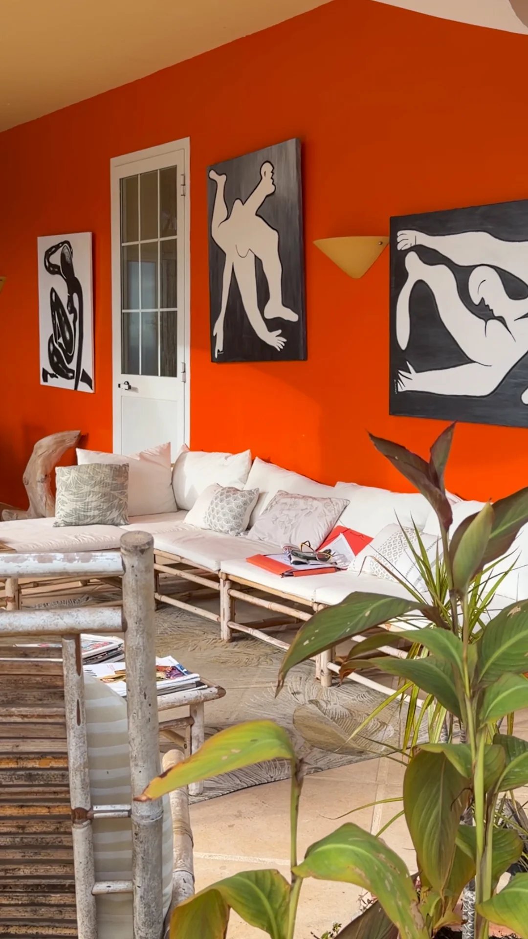 Intérieur d'une villa avec murs orange, œuvres d'art et mobilier en bambou.