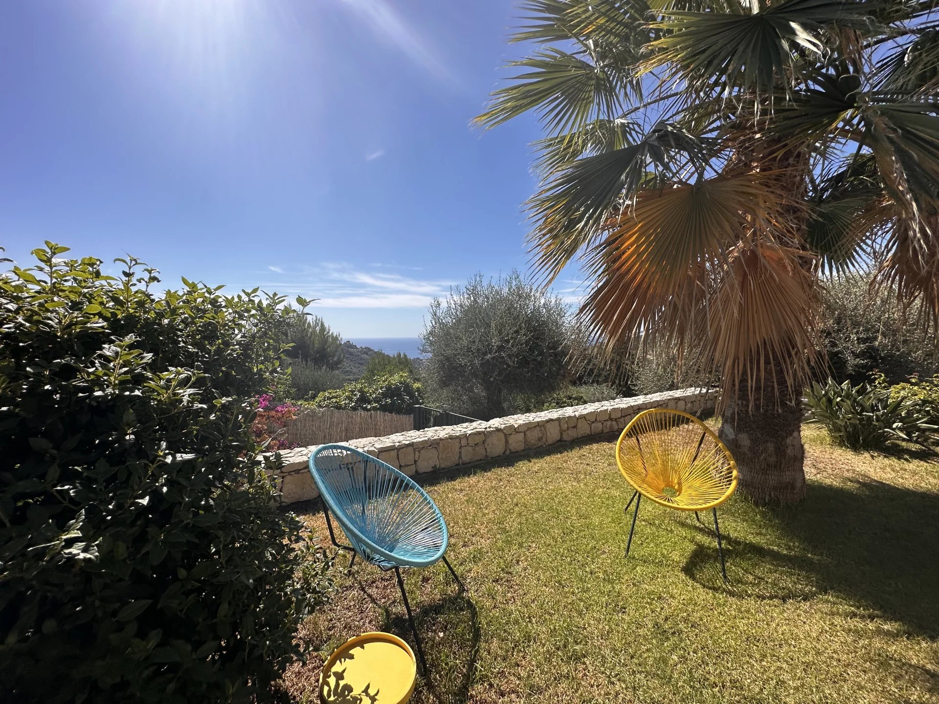 Jardin d'une villa avec chaises colorées et vue sur la mer, à Sainte-Agnès.