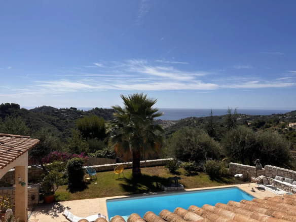 Vue d'une villa avec piscine et jardin, mer au loin, sous un ciel bleu.