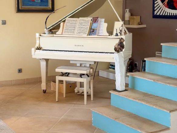 Intérieur d'une villa avec un piano blanc, un salon spacieux et des escaliers menant à un étage supérieur.