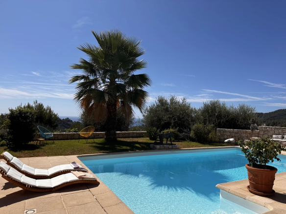 Piscine avec transats et palmiers dans un jardin, vue dégagée sur la mer et les montagnes.