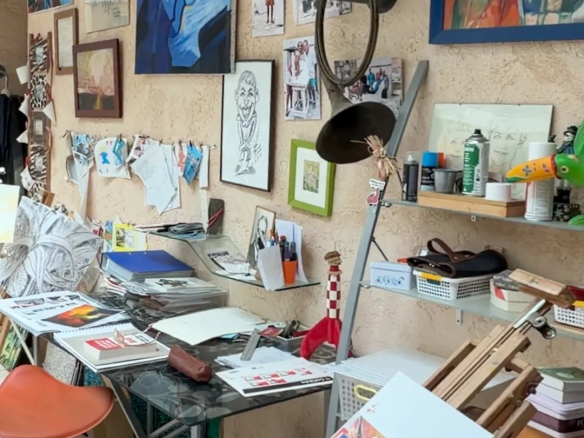 Atelier d'art avec tables, fournitures et œuvres accrochées au mur.