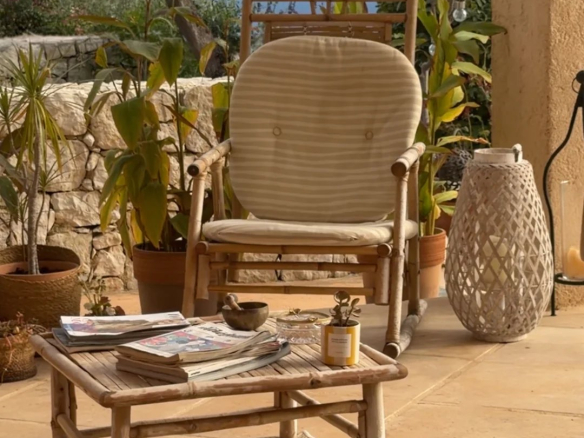 Terrasse d'une villa avec fauteuil, table basse, plantes et vue sur la mer.