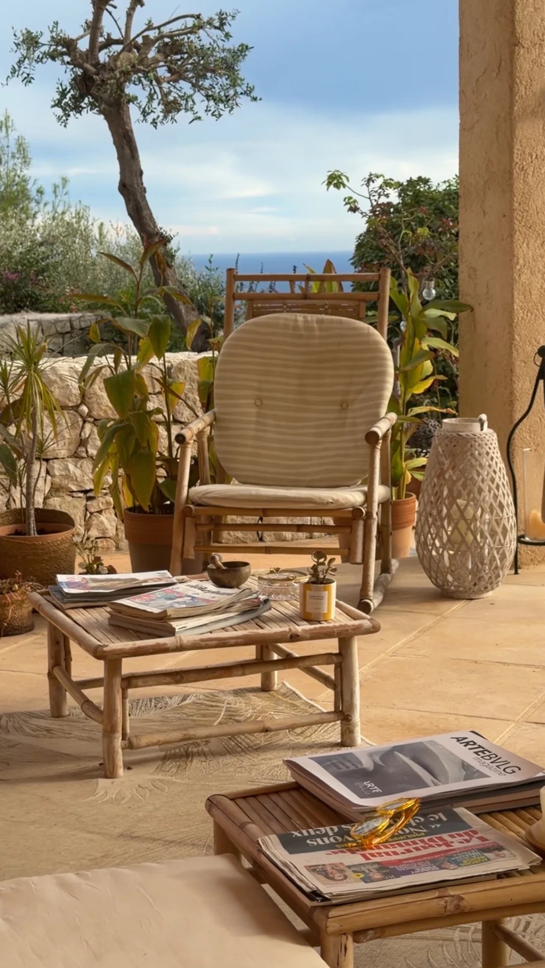 Terrasse d'une villa avec fauteuil, table basse, plantes et vue sur la mer.