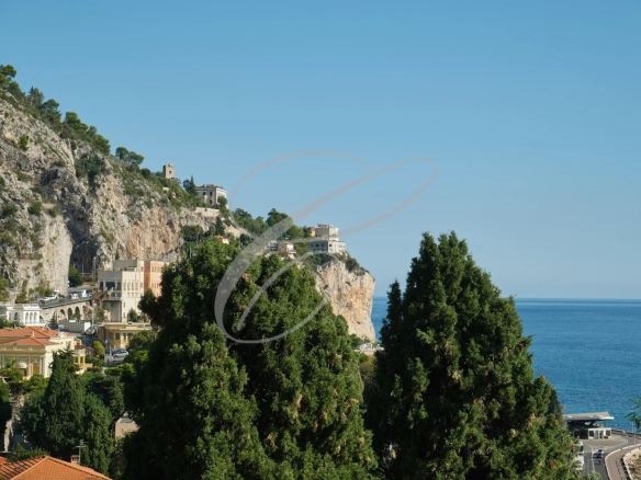 Vue panoramique de la mer et des collines à Menton Garavan, avec des arbres au premier plan.