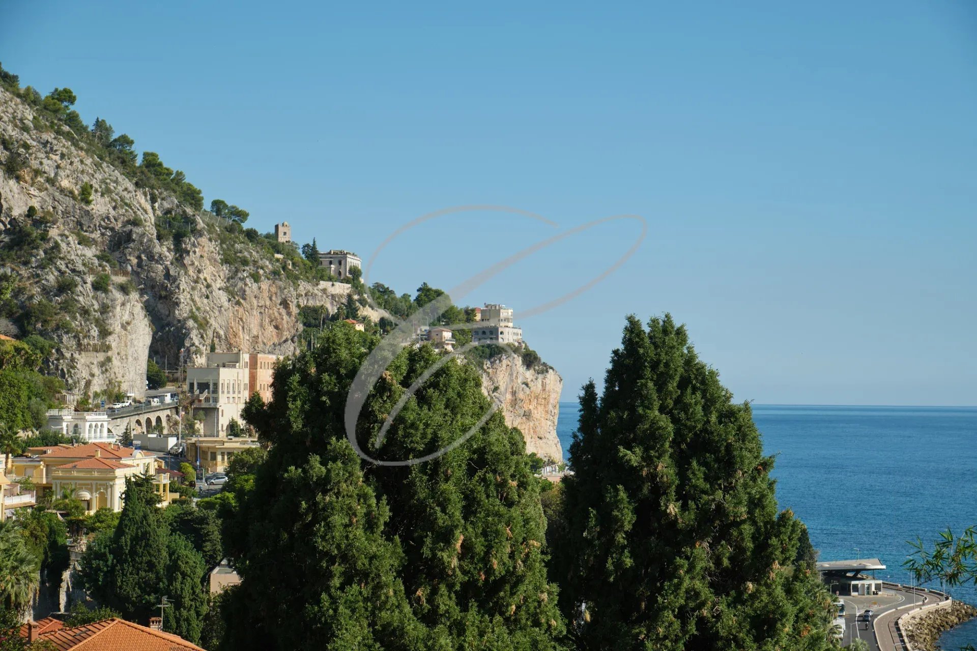 Vue panoramique de la mer et des collines à Menton Garavan, avec des arbres au premier plan.