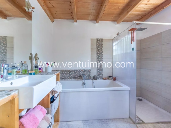Salle de bain moderne avec baignoire et douche, murs clairs et plafond en bois.