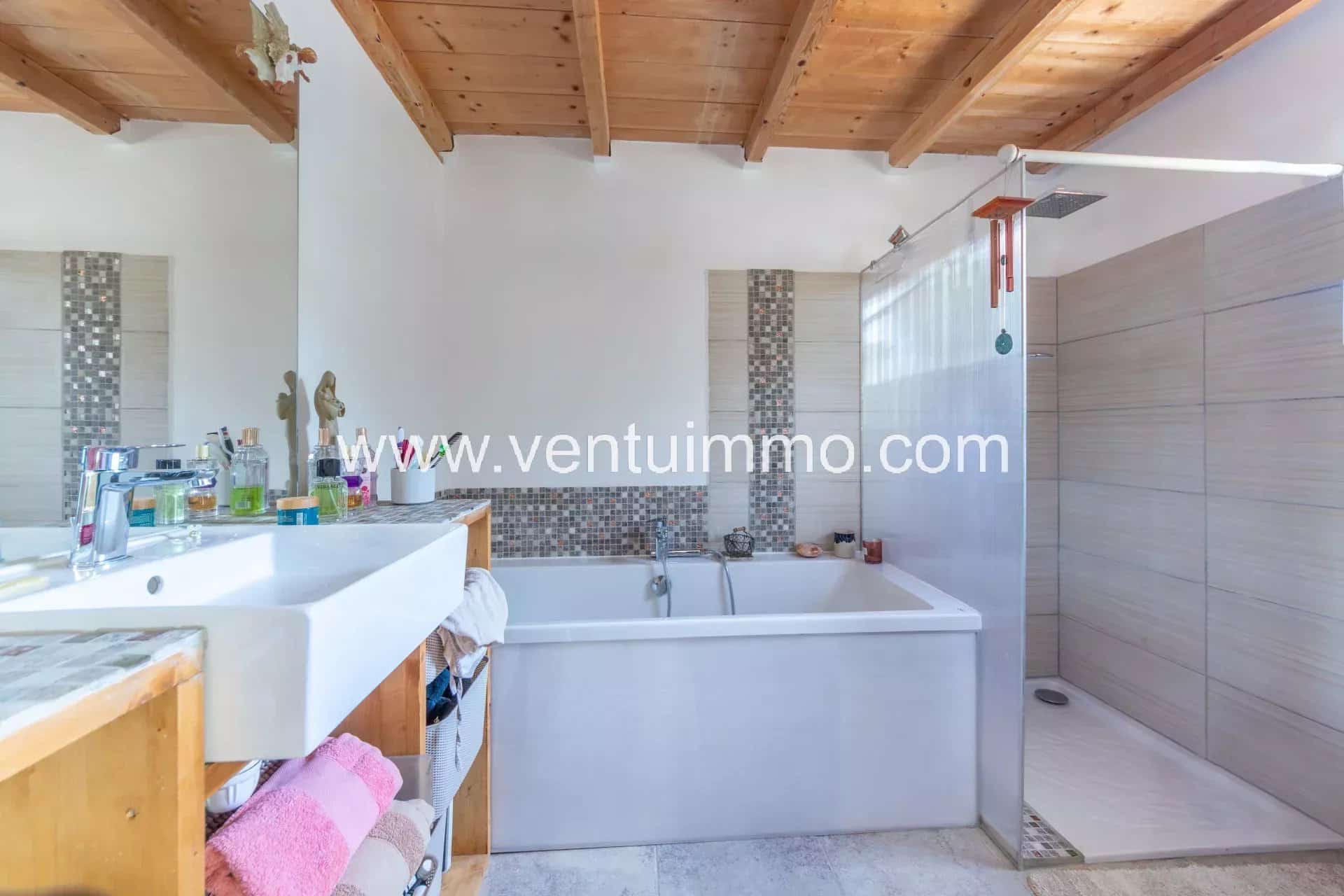 Salle de bain moderne avec baignoire et douche, murs clairs et plafond en bois.