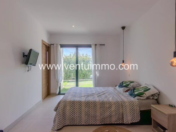 Chambre d'une villa moderne avec lit double et accès à un jardin fleuri.