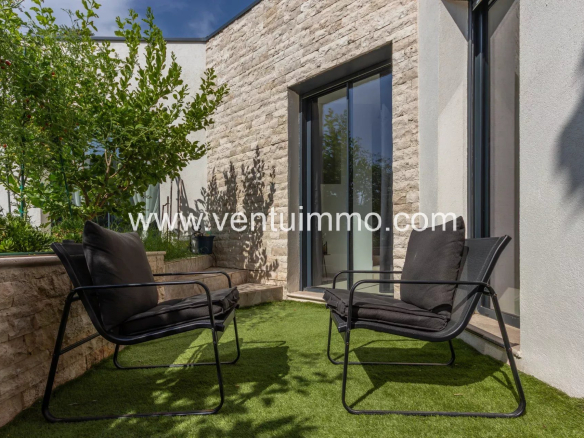 Espace extérieur d'une villa moderne avec chaises noires et jardin fleuri.