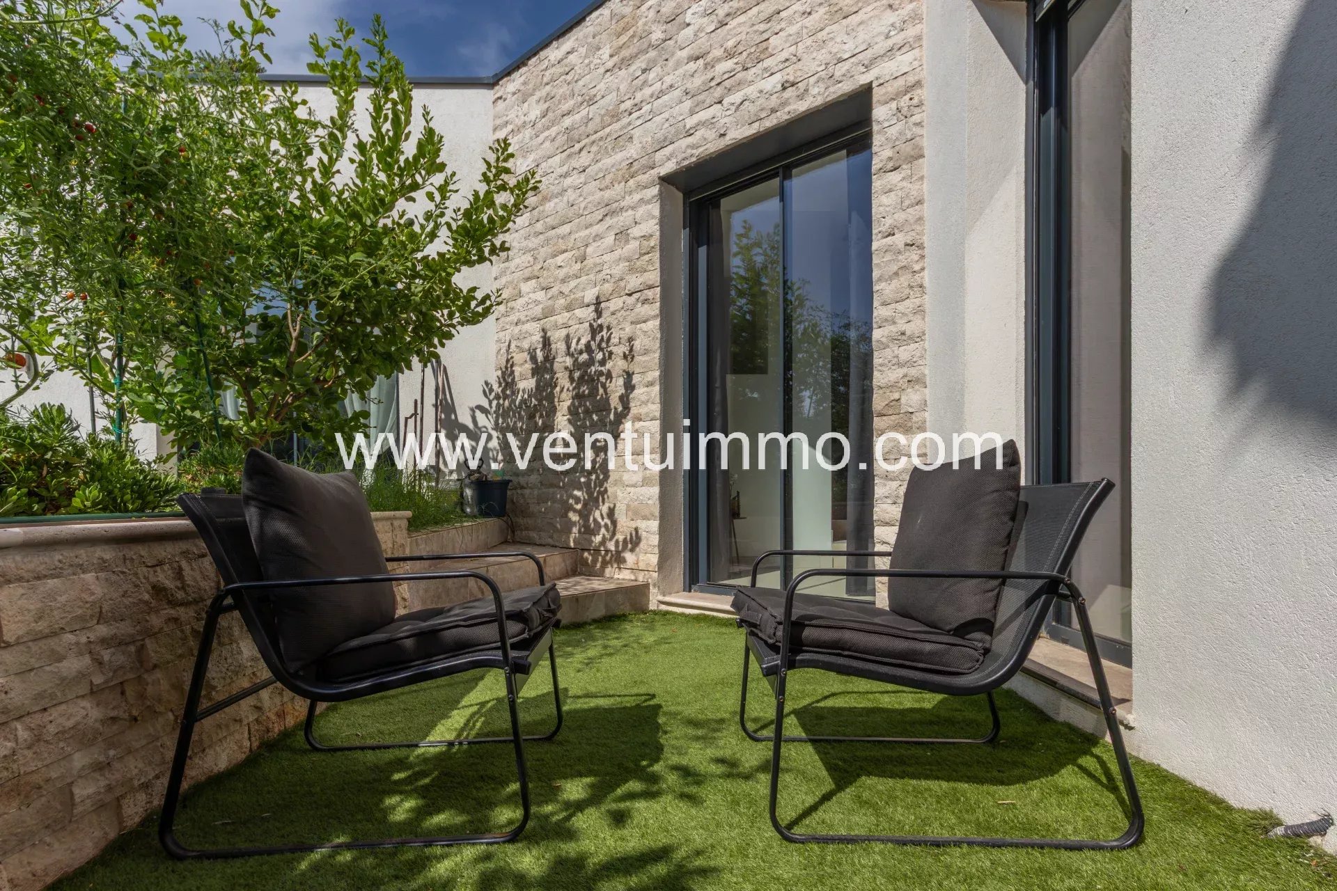 Espace extérieur d'une villa moderne avec chaises noires et jardin fleuri.