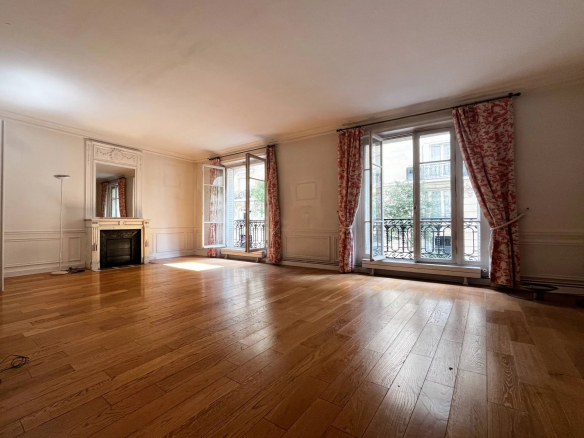 Intérieur d'un appartement familial à rénover avec parquet et moulures, fenêtres donnant sur un balcon.