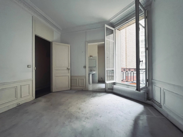 Intérieur d'un appartement à rénover avec fenêtres ouvertes, murs blancs et parquet.