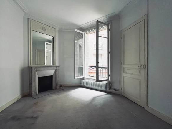 Intérieur d'un appartement à rénover avec fenêtres ouvertes, cheminée et murs blancs.