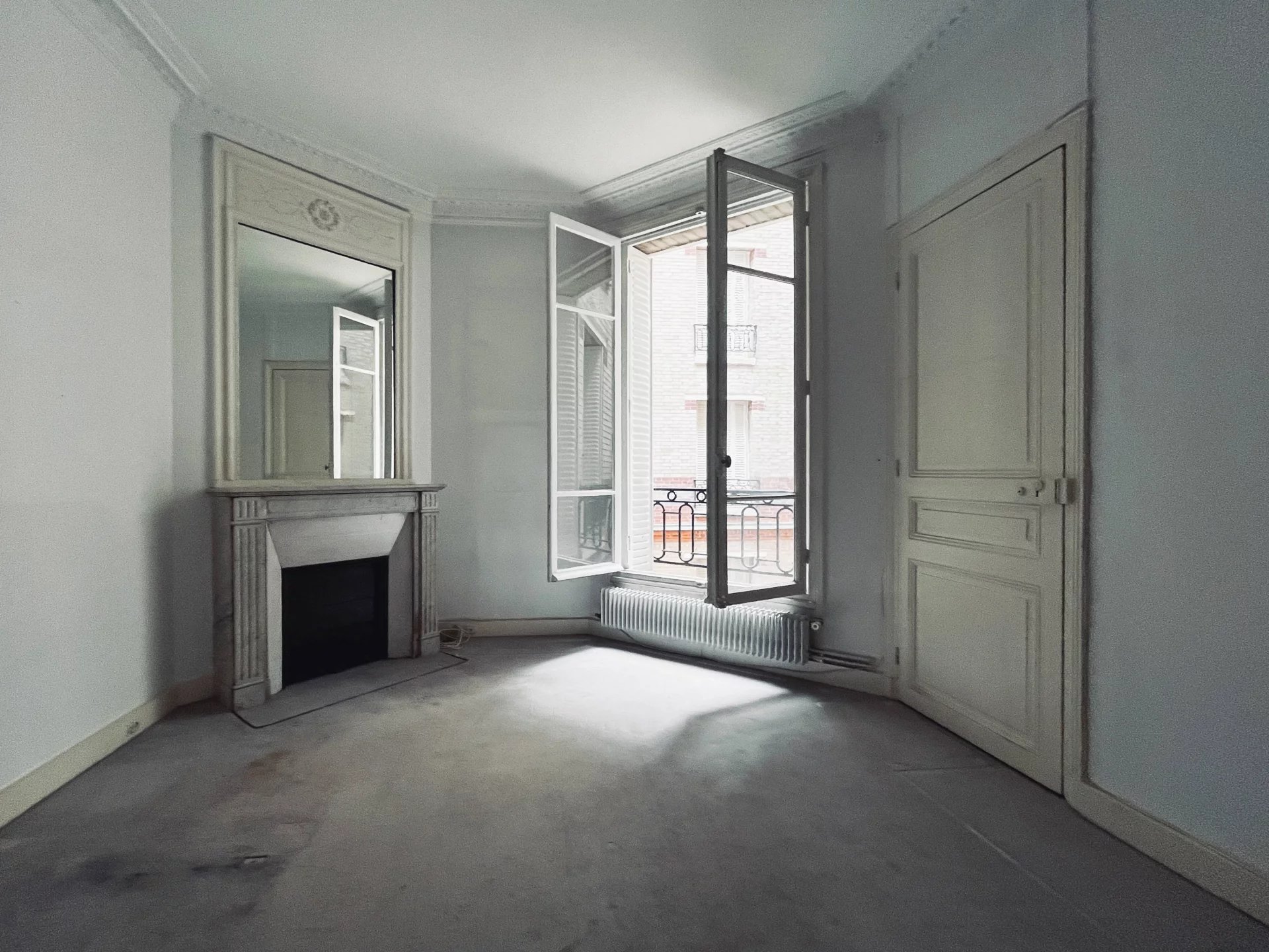 Appartement familial à rénover à Neuilly-sur-Seine Intérieur d'un appartement à rénover avec fenêtres ouvertes, cheminée et murs blancs.