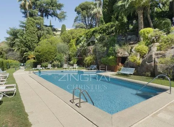 Piscine entourée de verdure dans une résidence à Cannes, avec chaises longues et palmiers.