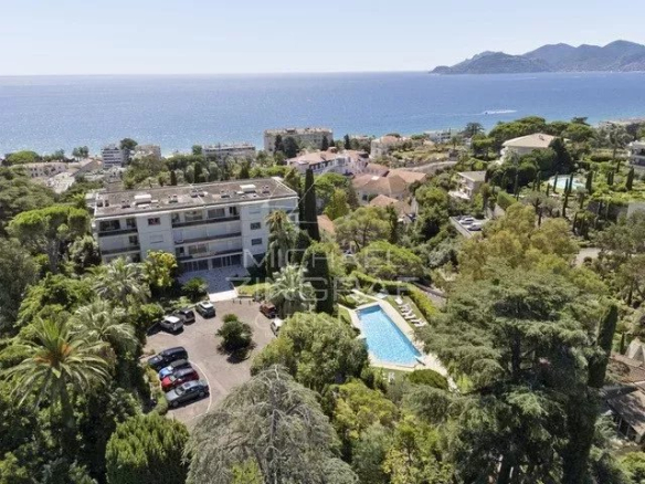 Vue aérienne d'une résidence avec piscine et parc à Cannes, entourée de verdure et proche de la mer.