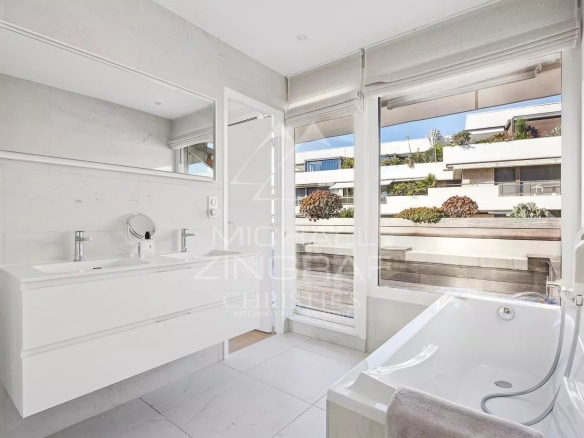 Salle de bain moderne avec baignoire et meuble vasque, lumière naturelle, vue sur l'extérieur.