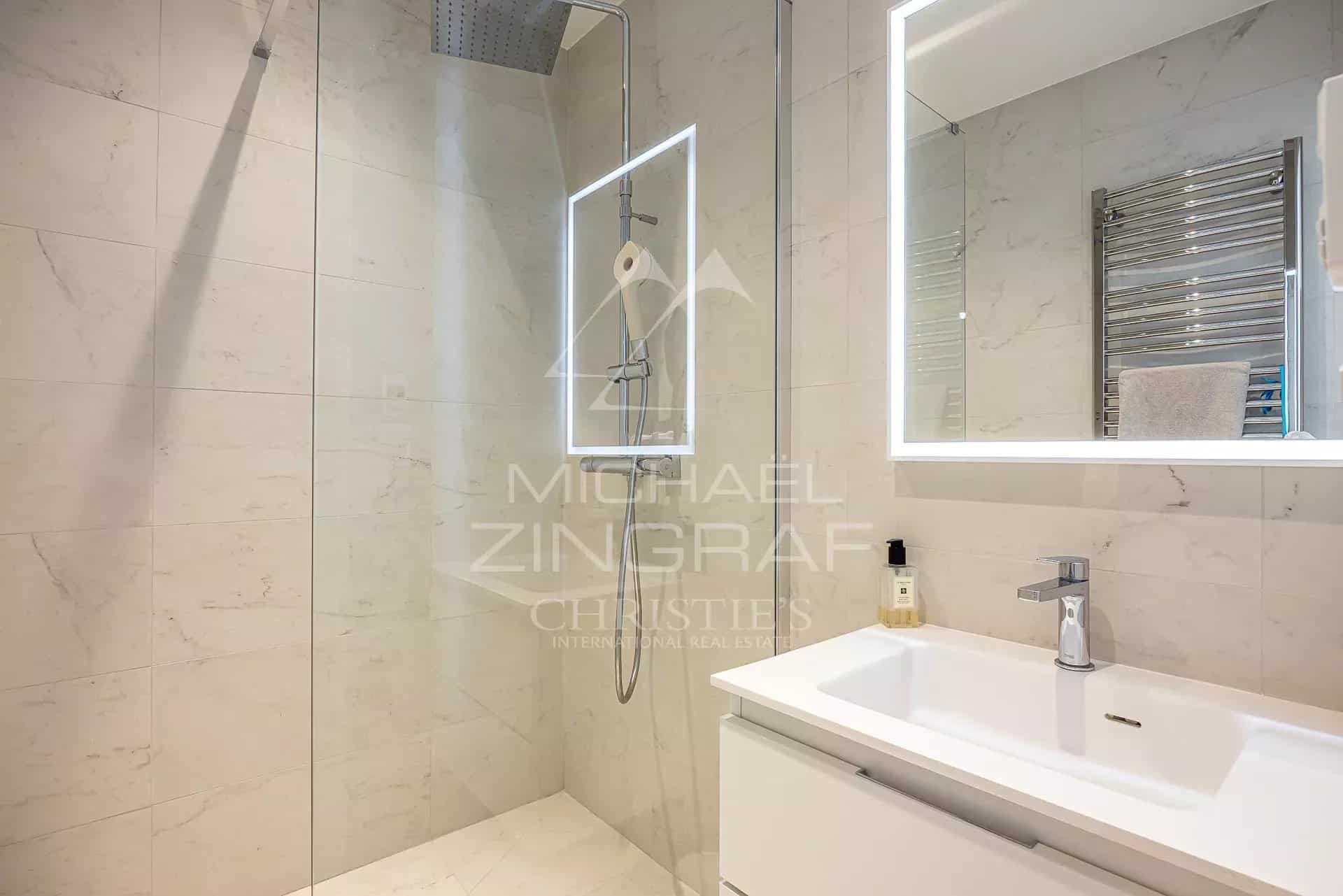 Salle de bain moderne avec douche à l'italienne et lavabo, murs en carrelage clair.