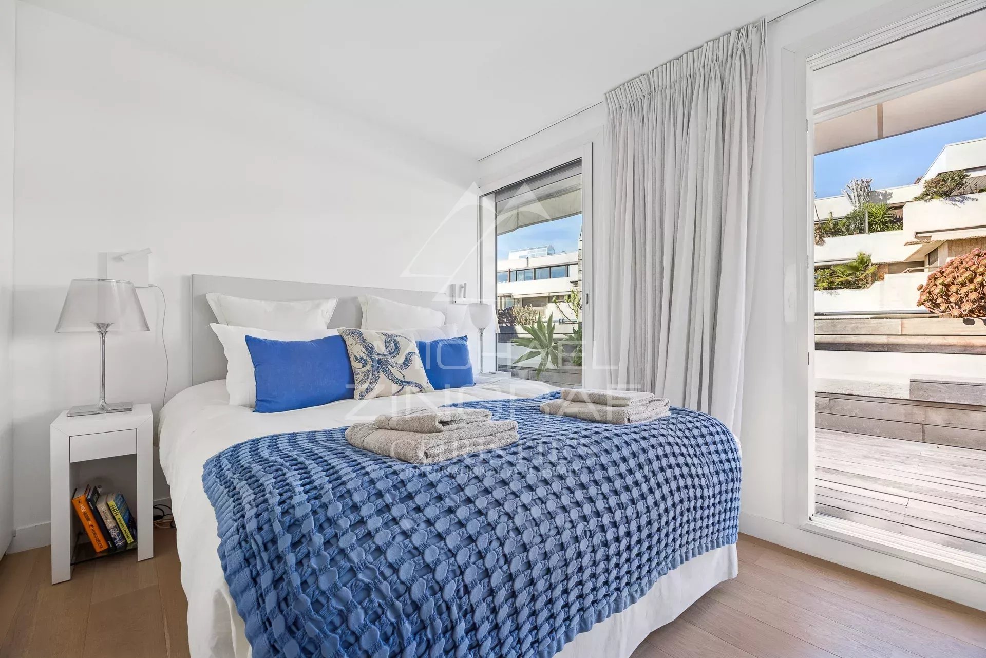 Chambre d'un appartement moderne avec literie bleue et accès à une terrasse.