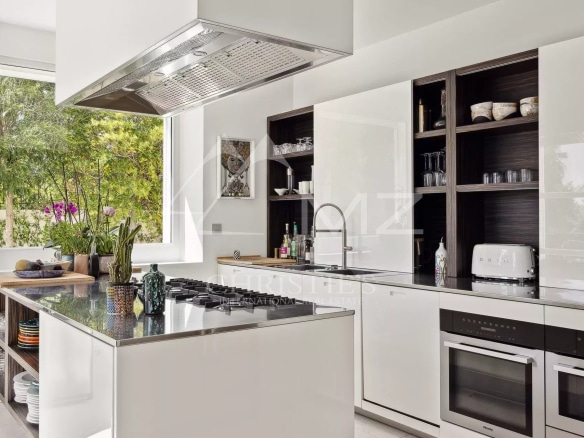 Modern kitchen with central island and windows overlooking greenery.