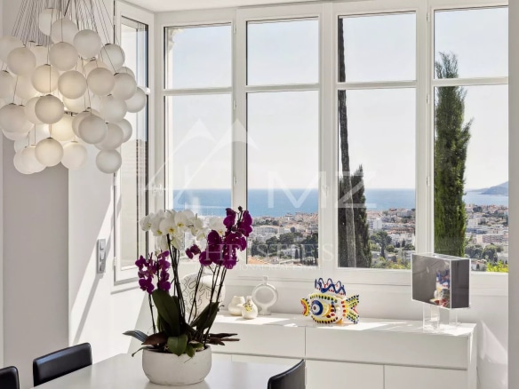 Panoramic sea view from a renovated villa, with flowers and modern decor inside.