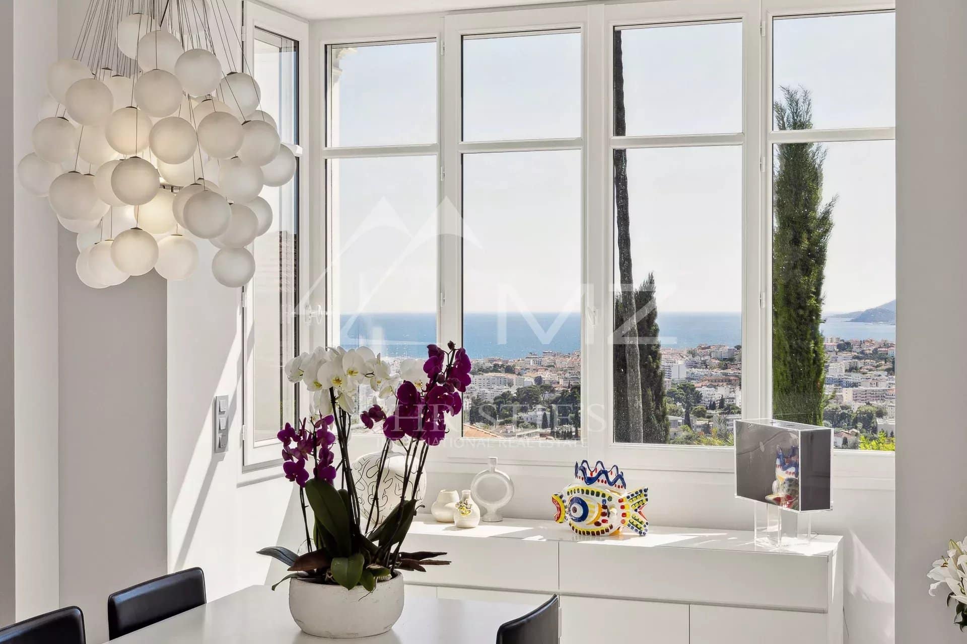 Panoramic sea view from a renovated villa, with flowers and modern decor inside.