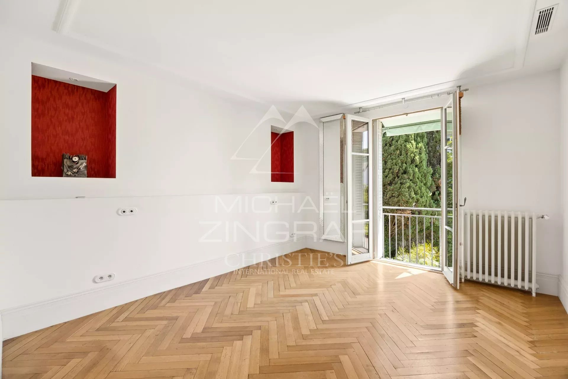 Intérieur d'une maison à Cannes avec parquet en bois et fenêtres ouvertes sur un jardin.