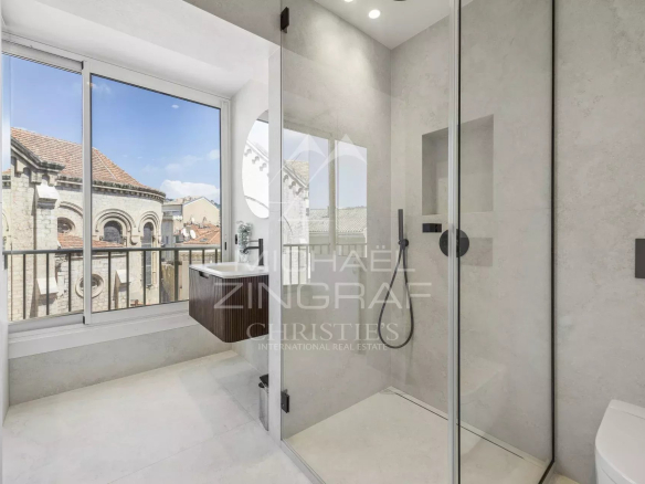 Salle de bain moderne avec douche et fenêtre, vue sur des bâtiments historiques à Cannes.