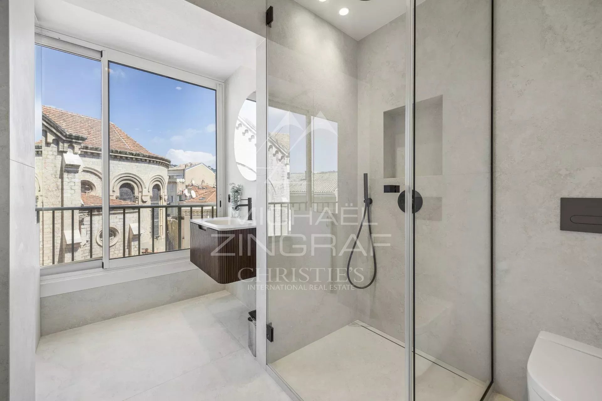 Salle de bain moderne à Cannes Salle de bain moderne avec douche et fenêtre, vue sur des bâtiments historiques à Cannes.