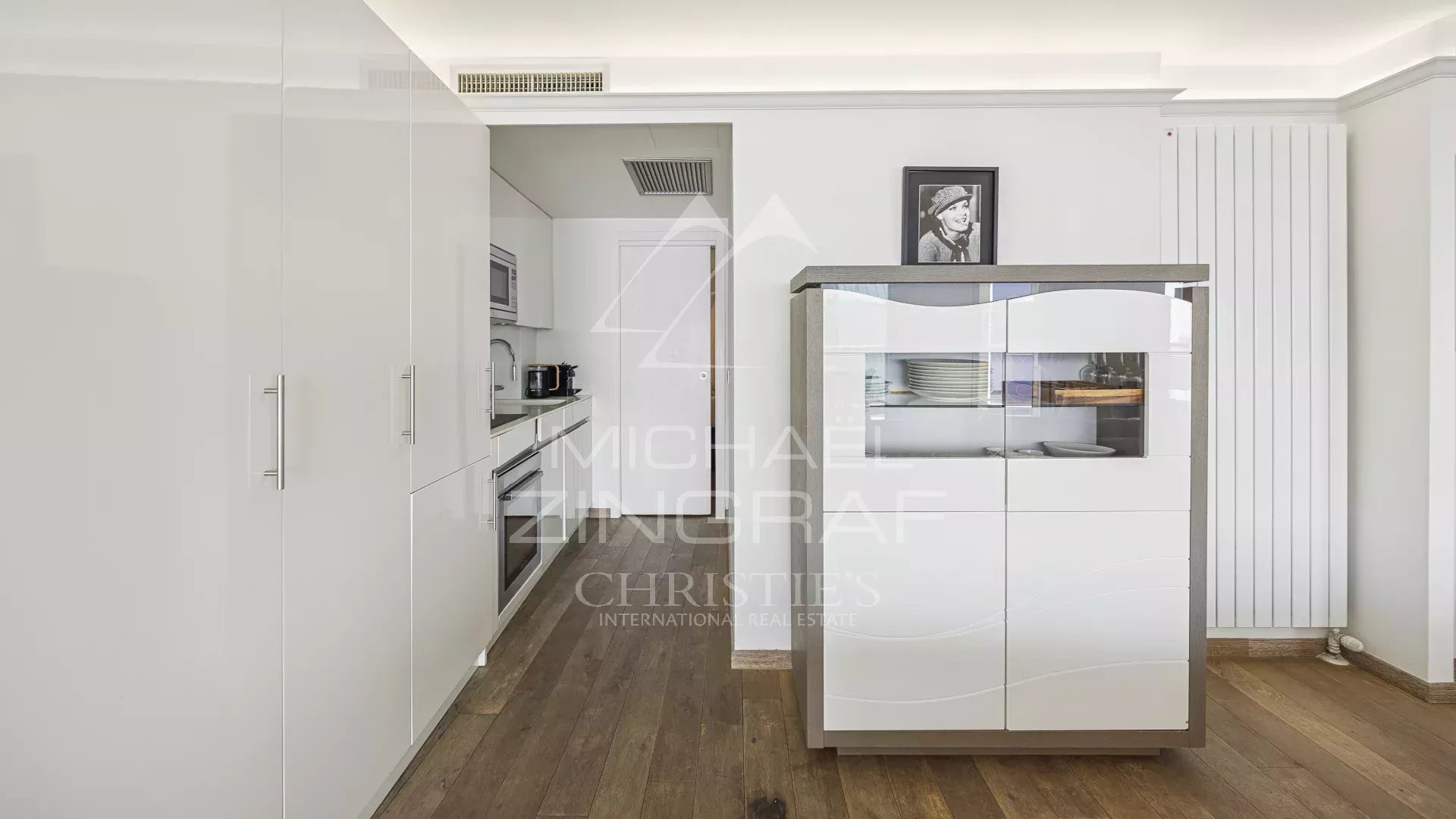 Cuisine d’un appartement à Cannes Cuisine moderne avec meubles blancs et espace de rangement, vue sur le séjour lumineux.