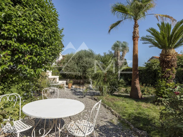 Jardin paysager d'une villa bourgeoise à Cannes, avec table et chaises, palmiers et verdure.