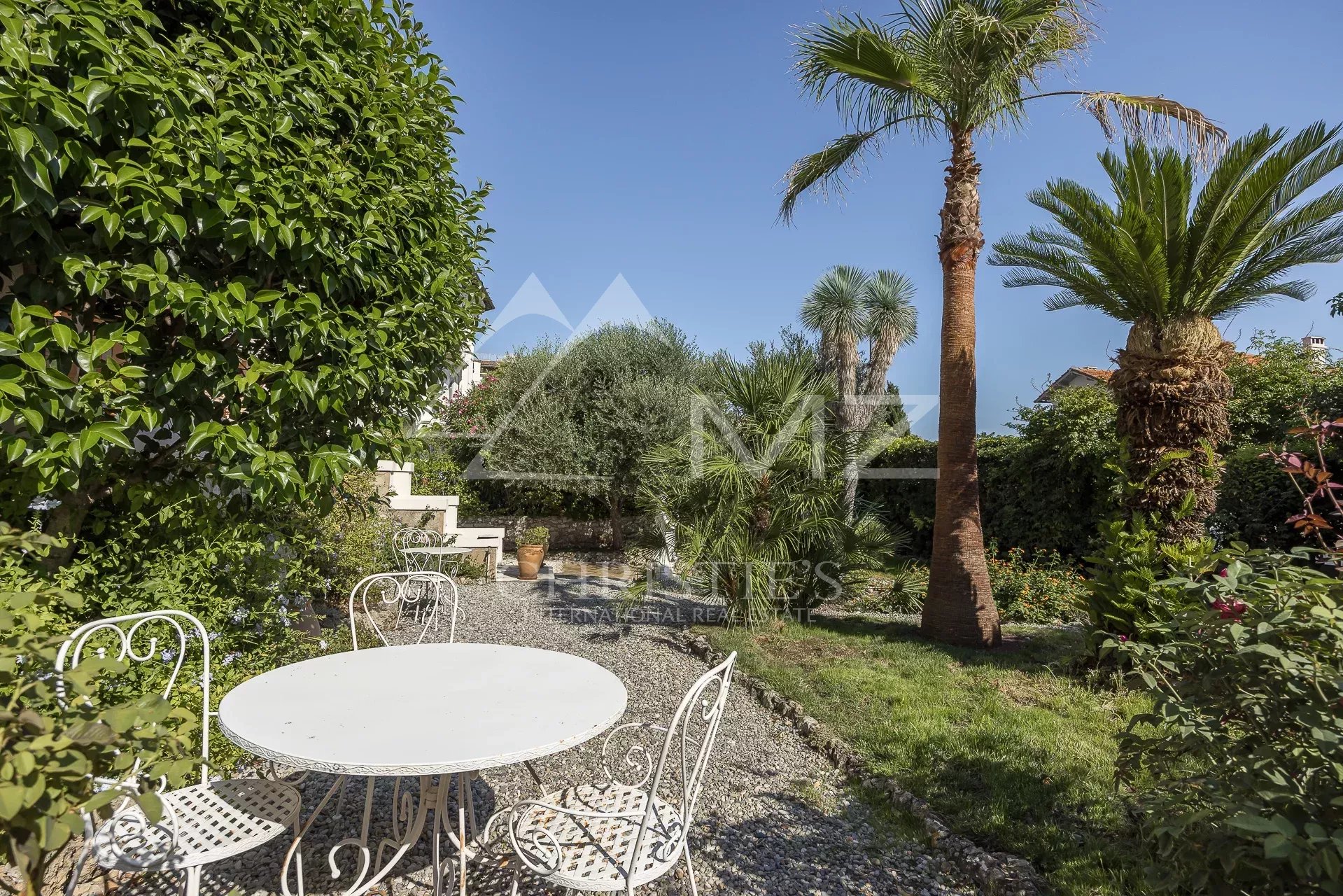 Jardin de la villa bourgeoise à Cannes Jardin paysager d'une villa bourgeoise à Cannes, avec table et chaises, palmiers et verdure.