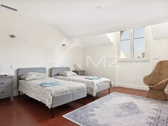 Chambre avec deux lits simples, fenêtre et fauteuil en osier, dans une villa bourgeoise à Cannes.