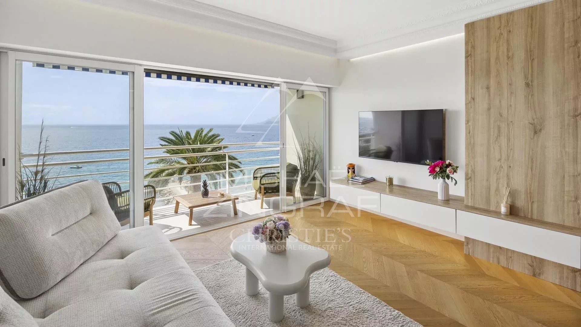 Intérieur d'un appartement moderne avec vue sur la mer, canapé et télévision.